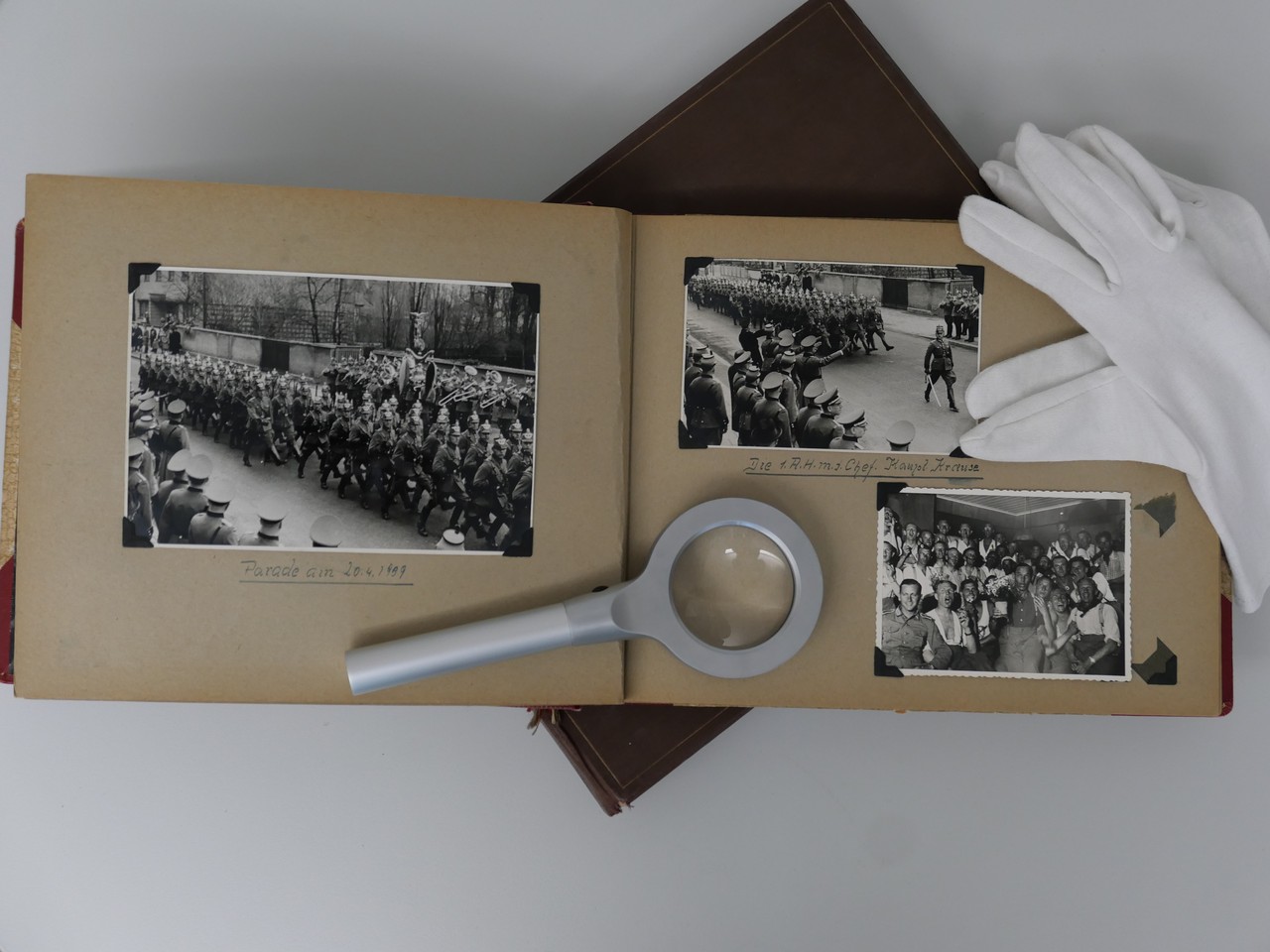 Ein Fotoalbum mit schwarz-weißen Fotos liegt aufgeschlagen auf einem Tich, darauf liegen weiße Handschuhe und eine Lupe. Ein Fotoalbum mit schwarz-weißen Fotos liegt aufgeschlagen auf einem Tich, darauf liegen weiße Handschuhe und eine Lupe.